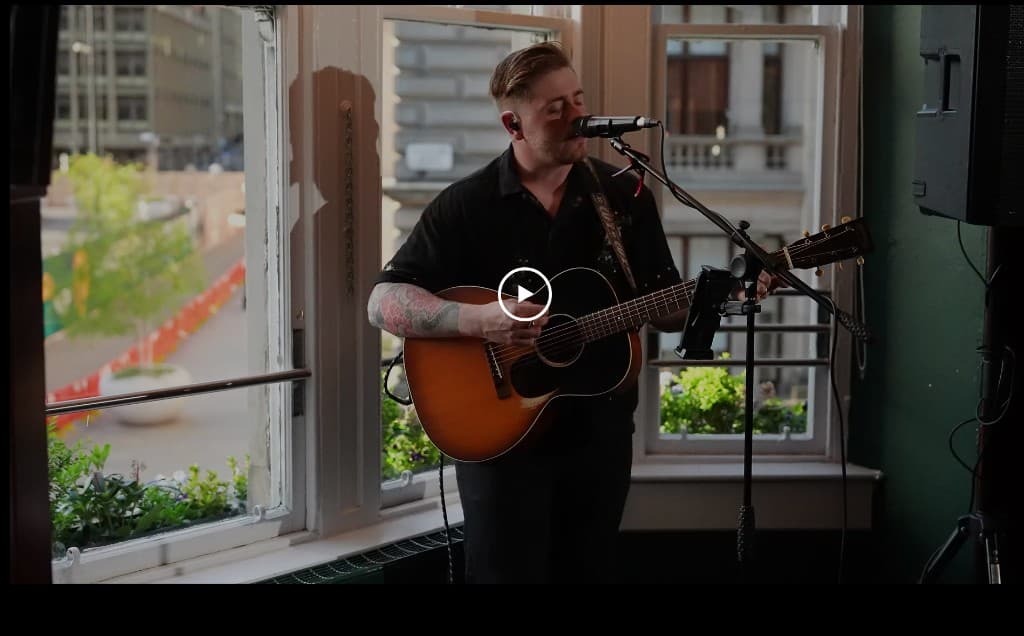 Calum performing acoustic guitar at a sunlit window